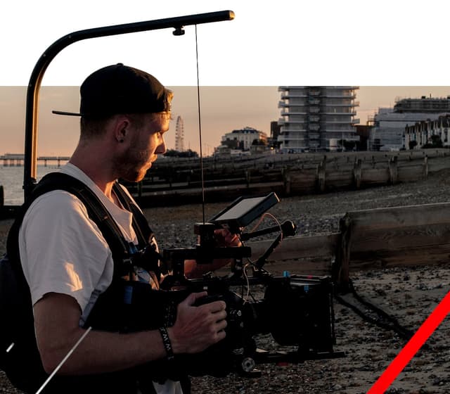 Man with camera rig filming city`s beach at sunset